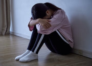 Person sitting on the floor with head in hands against a white wall.